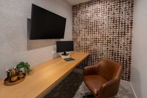 A brown leather chair sits in front of a desk with a black monitor and a lamp.