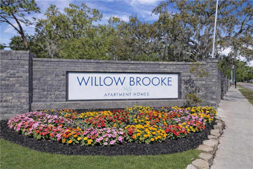 A sign for Willowbrooke Apartment Homes is framed by a flower bed. at Willow Brooke Apartments, Tampa, 33613