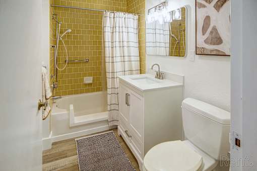 A bathroom with a yellow tiled shower area and a white toilet.