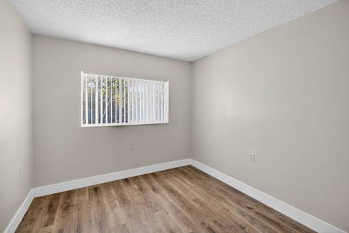 A room with wooden flooring and a window with blinds.