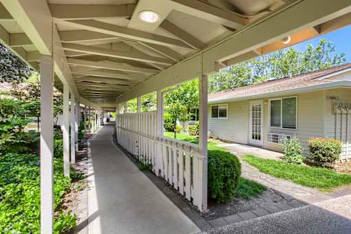 A long white porch with a white railing and a white house with a green lawn.
