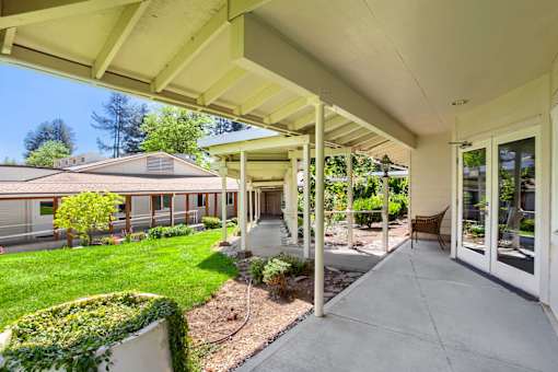 A covered walkway leads to a building with a brown chair on the right.