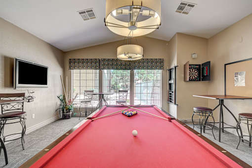 A pool table in a room with a television, chairs, and a dartboard.