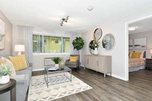 A well-lit living room with a grey couch, a coffee table, and a large mirror on the wall.