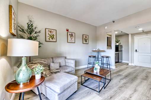 A living room with a grey couch, a wooden coffee table, and a green vase on a wooden table.