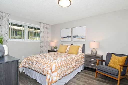 A bedroom with a patterned bedspread and a grey chair.