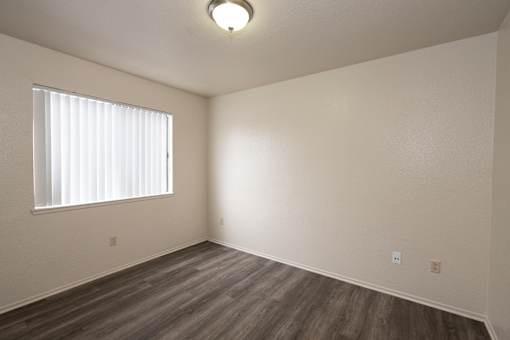 A room with a window covered by white blinds and wooden flooring.