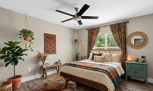 A bedroom with a bed, a ceiling fan, and a window with curtains.