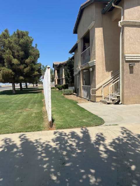 A white sign is leaning against a tree in front of a building.