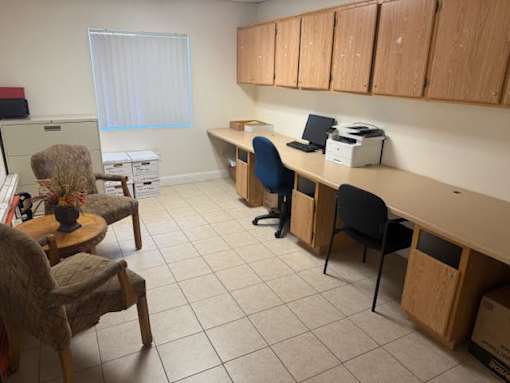 A room with a desk, chairs, and a printer.