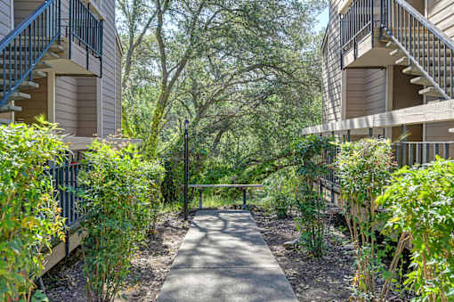 A pathway leads through a landscaped courtyard between two apartment buildings.