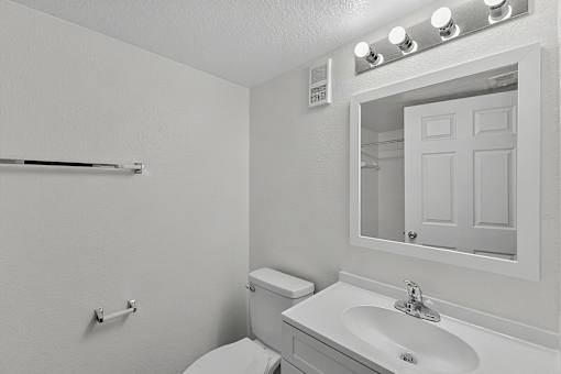 A white bathroom with a toilet, sink, mirror and lights.