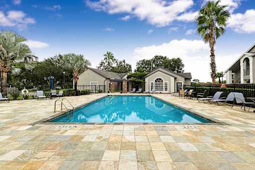 A pool surrounded by a tiled patio and lounge chairs.