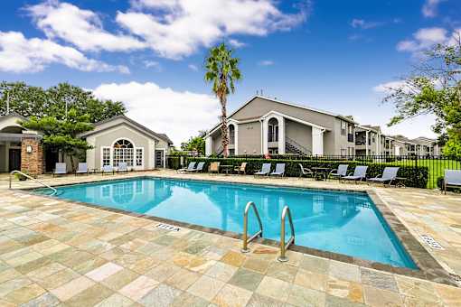 A swimming pool surrounded by lounge chairs and palm trees.