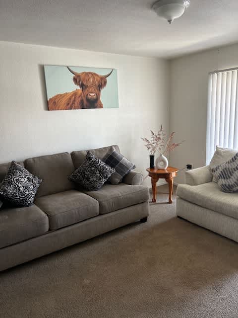 A living room with a grey couch and a cow picture on the wall.