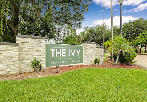 A sign that says "The Ivy Apartment Homes" in front of a stone wall.