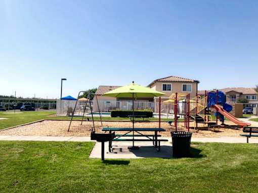 A playground with a green umbrella and a slide.