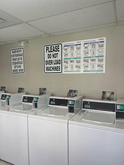 A row of washing machines with a sign above them that says "Please do not over load machines".