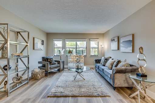 A living room with a grey couch, a glass coffee table, and a rug.
