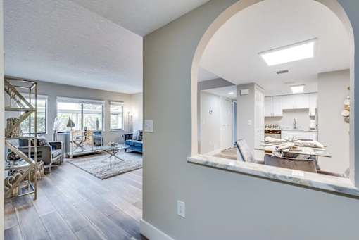 A living room with a large window and a view of the kitchen.