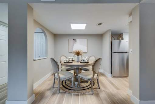 A dining room with a table set for two and a refrigerator in the corner.