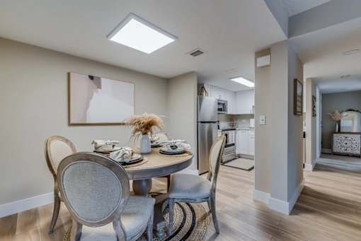 A dining room with a table set for two and a kitchen in the background.