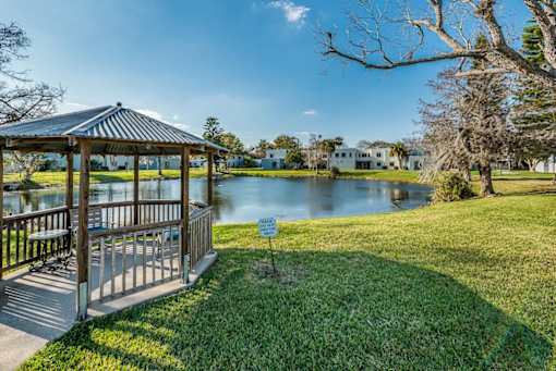 A gazebo sits in a grassy area next to a lake.