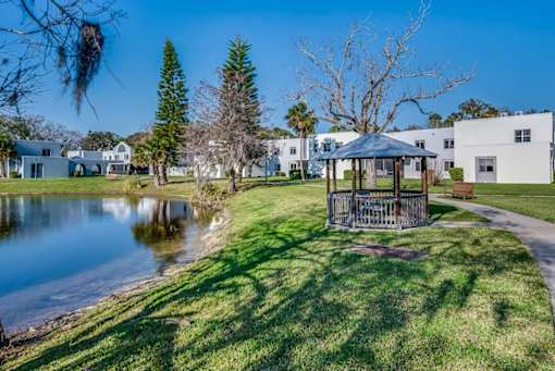 A gazebo sits in the middle of a grassy area next to a pond.