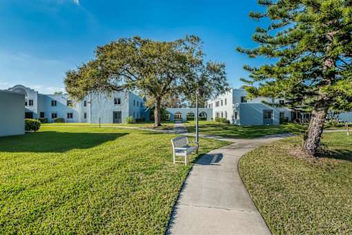 A white bench sits on a concrete path in front of a white building.