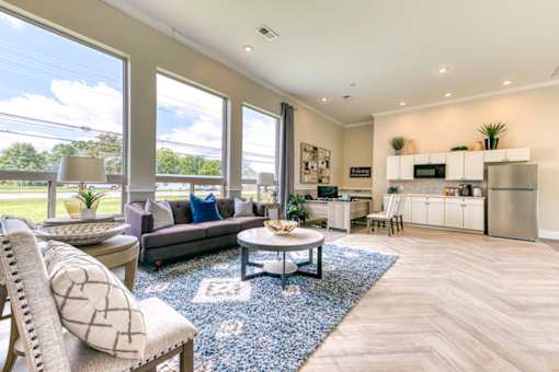 A well-lit, spacious living room with a grey sofa, a round coffee table, and a large window.