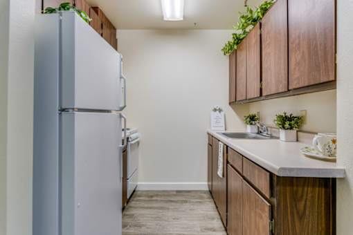 A kitchen with a refrigerator, wooden cabinets, and a sink.
