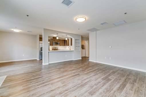 A spacious room with wooden flooring and a kitchen area in the background.