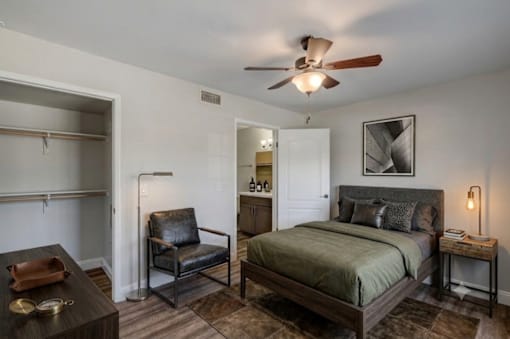 A bedroom with a bed, chair, and a ceiling fan.