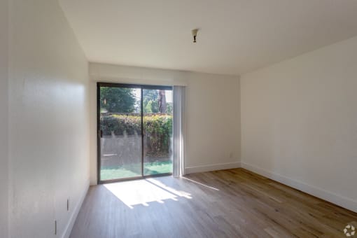an empty living room with a sliding glass door to a backyard