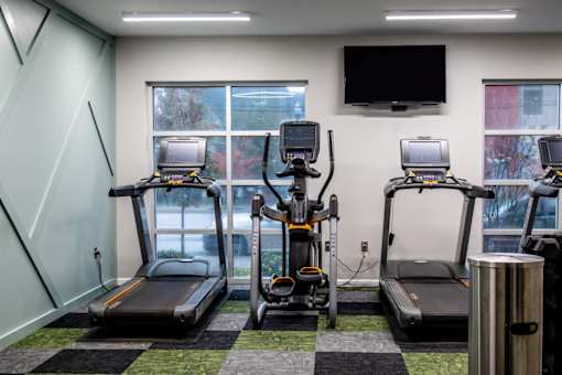 a gym with four treadmills and a tv on the wall