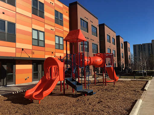 A playground with a red slide in front of a building.