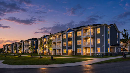 A row of apartment buildings are lit up at dusk.