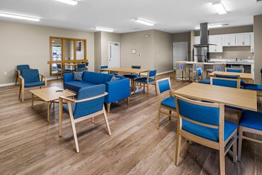 a common room with tables and chairs and a kitchen