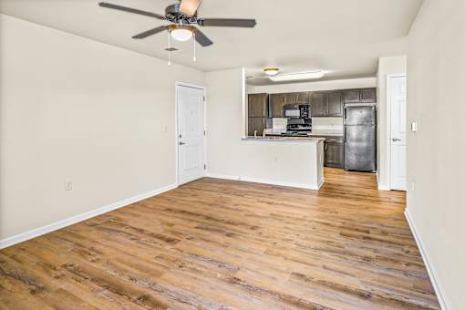 an empty living room with wood flooring and a kitchen