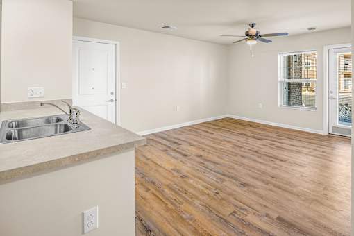 an empty living room with a kitchen and a ceiling fan
