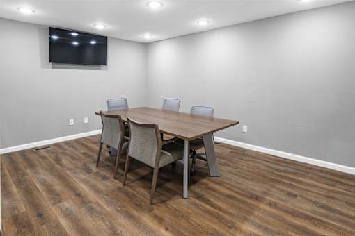 A conference room with a table and chairs and a television on the wall.