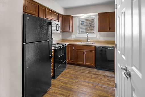 A black refrigerator stands in a kitchen with wooden floors and brown cabinets.