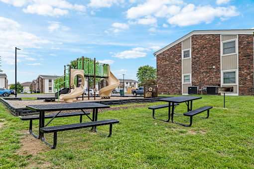 A playground with a slide and picnic tables in front of a brick building.
