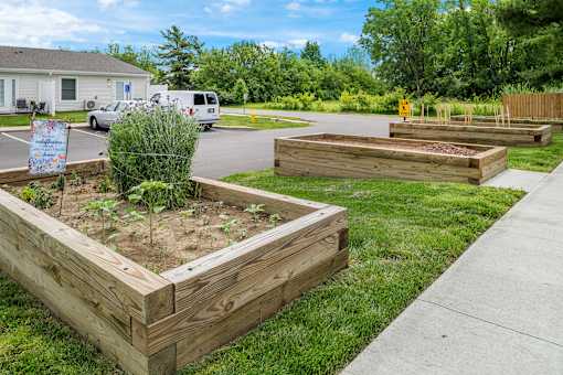 A wooden raised garden bed with a sign in front of a white building.