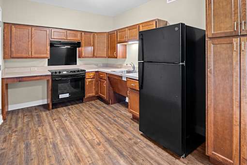 A black refrigerator stands in a kitchen with wooden cabinets and a black stove.