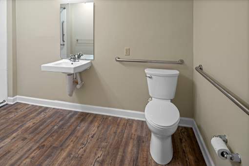 A white toilet sits in a bathroom with wood flooring.