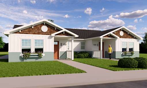 A woman stands in front of a two-story house with a brown roof and white walls.