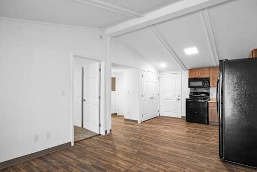 A kitchen area with a black fridge, white walls, and wooden floors.