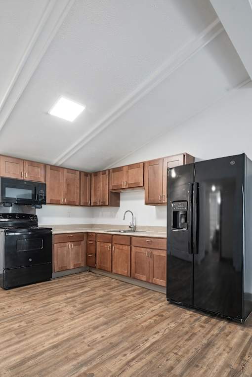 A black refrigerator stands in a kitchen with wooden cabinets.