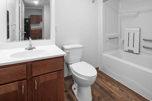 A white toilet sits in a bathroom with wooden cabinets and a white sink.